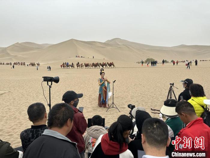 圖為2023年4月底，敦煌大漠“逐舞者”奧楠在鳴沙山月牙泉景區(qū)視頻直播，吸引游人圍觀?！●T志軍 攝